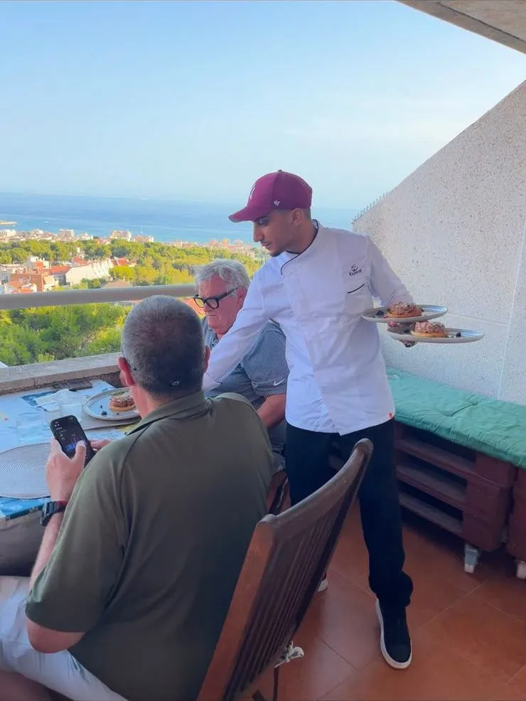 Moneim sirviendo los platos en una terraza frente al mar